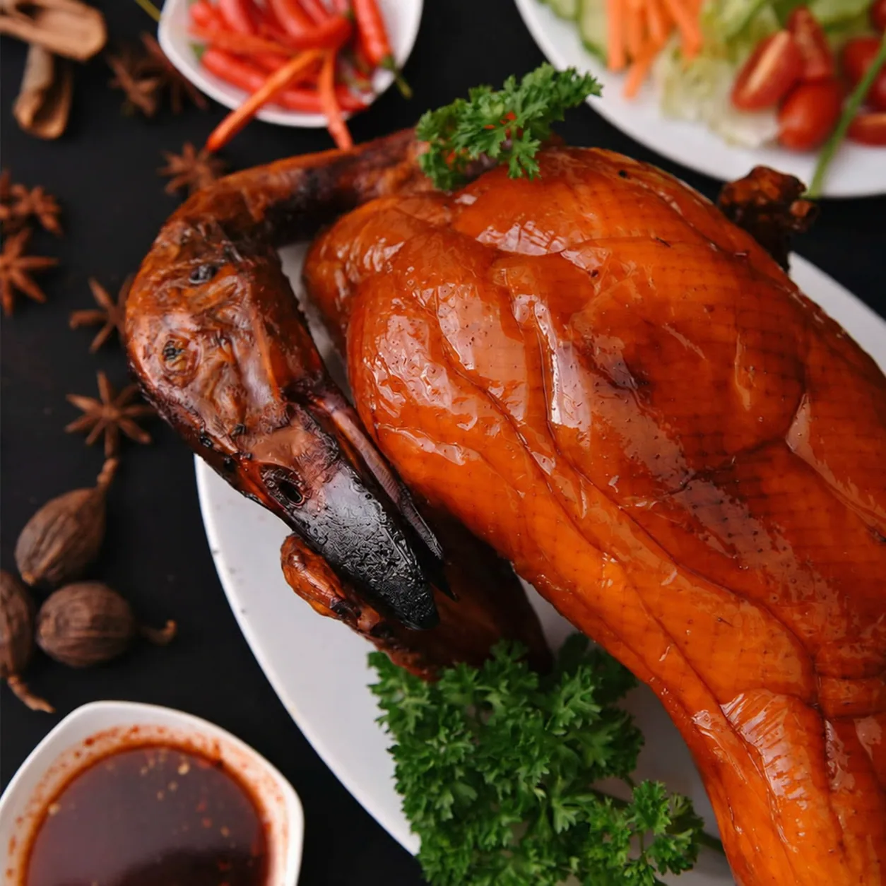 Vịt quay Quảng Đông nguyên con, da bóng nâu cam, bày trên đĩa cùng gia vị và nước chấm